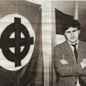 Gianni Alemanno posiert vor einer Fahne mit dem rassistischen Keltenkreuz-Symbol.